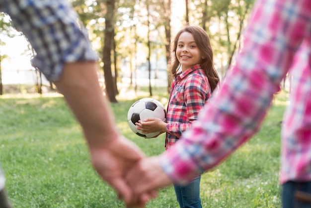 De het voetbalbal die van het meisjesholding haar ouderholding bekijkt dient park in