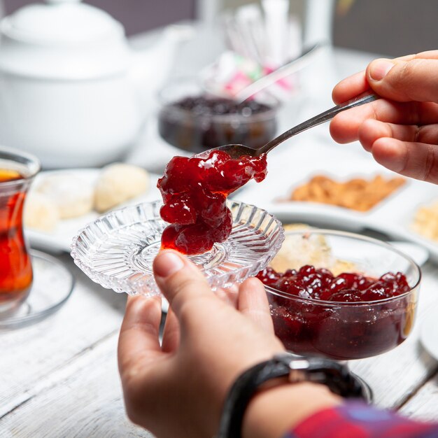 De hoge mens die van de hoekmening heerlijke fruitjam met thee, noten op witte houten achtergrond dient.