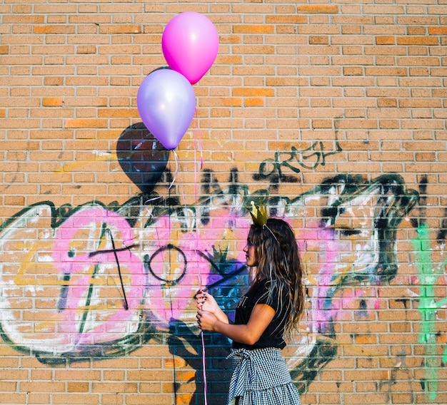 Gratis foto de holdingsballons van het meisje voor graffitimuur