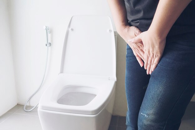 De holdingshand van de vrouw dichtbij toiletkom - het concept van het gezondheidsprobleem