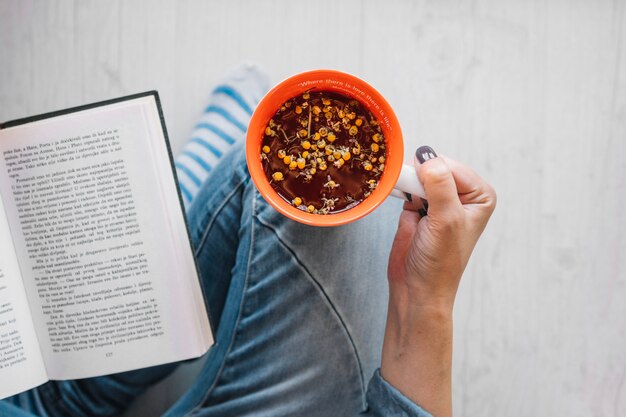 De holdingskop van de vrouw met thee dichtbij boek