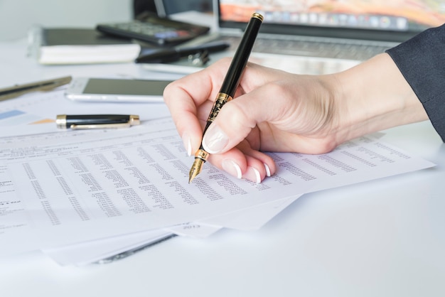 Gratis foto de holdingspen van de vrouwenhand bij bureau met documenten