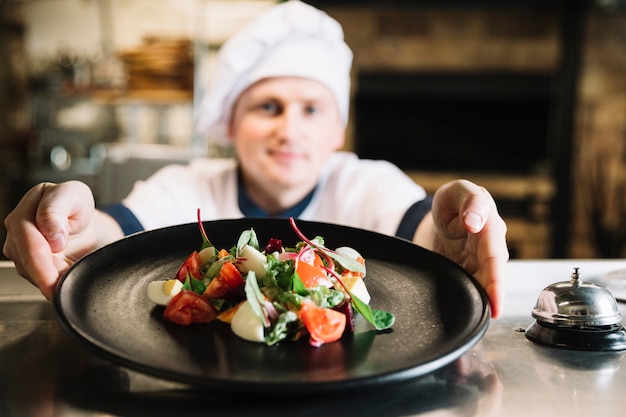 De holdingsplaat van de kok met salade dichtbij de dienstklok