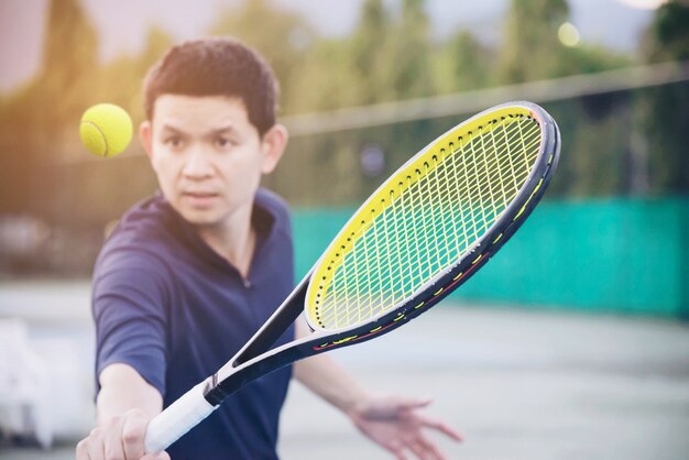 De holdingsracket van de mens ongeveer om een bal in tennisbaan te raken