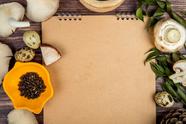 De hoogste mening van verse de kwartelseieren van paddestoelen zwarte peperbollen schikte rond een schetsboek op rustiek hout