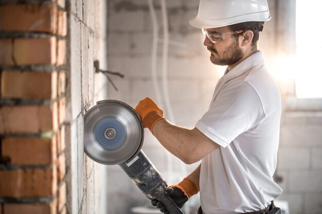 De industriële bouwer werkt met een professionele haakse slijper om stenen te snijden en binnenmuren te bouwen. Elektricien.