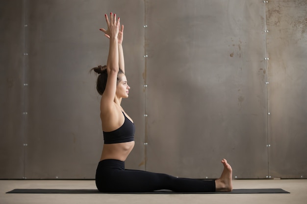 De jonge aantrekkelijke vrouwenzitting in dandasana stelt, grijze studiobedelaars