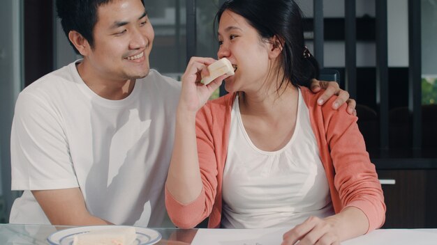 De jonge Aziatische Zwangere baby van de vrouwentekening in buik en familie in notitieboekje. Papa die sandwich geeft zijn vrouw terwijl het gelukkige positief en vreedzame glimlachen terwijl zorgkind op lijst thuis in woonkamer neemt.