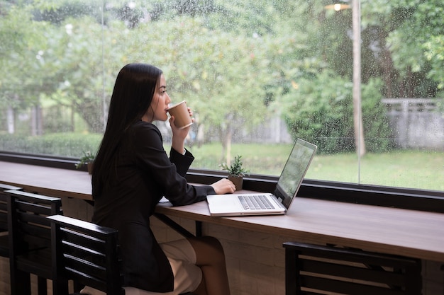 De jonge bedrijfsvrouw heeft een onderbreking met koffie terwijl het werken aan laptop in het bureau