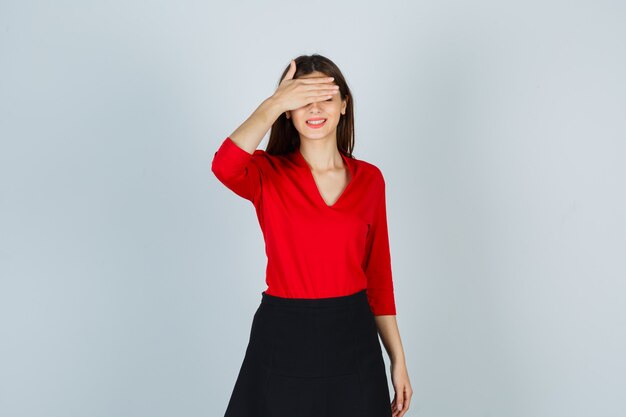 De jonge dame die ogen behandelt dient rode blouse, zwarte rok in en kijkt vrolijk