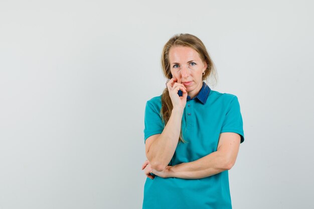 De jonge dame die zich in het denken bevindt stelt in t-shirt en kijkt verstandig