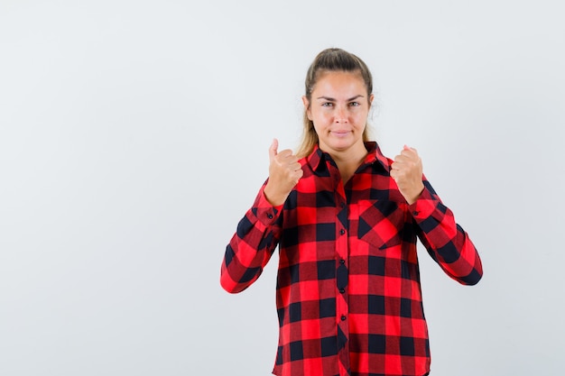 De jonge dame die zich in strijd bevindt stelt in casual overhemd en kijkt zelfverzekerd, vooraanzicht.