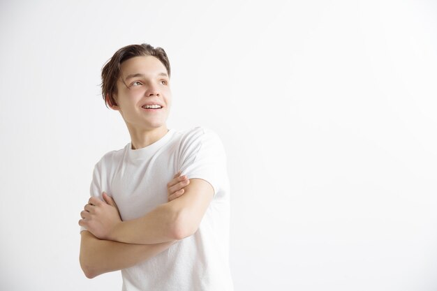 De jonge dromende glimlachende tiener wacht op chanses die op grijze achtergrond worden geïsoleerd. Dromer bij studio in wit T-shirt met met het romantische zicht en gekruiste handen.
