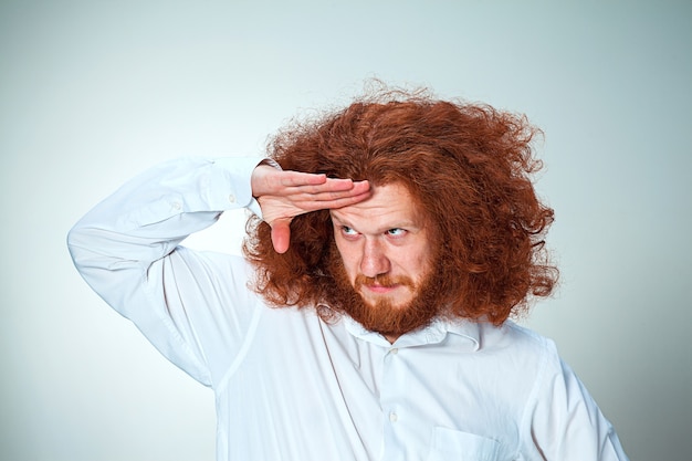 De jonge glimlachende man met lang rood haar die speels wegkijkt