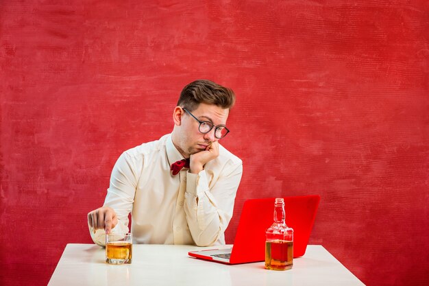 De jonge grappige man met cognac zittend met laptop op St. Valentijnsdag op rode studio.