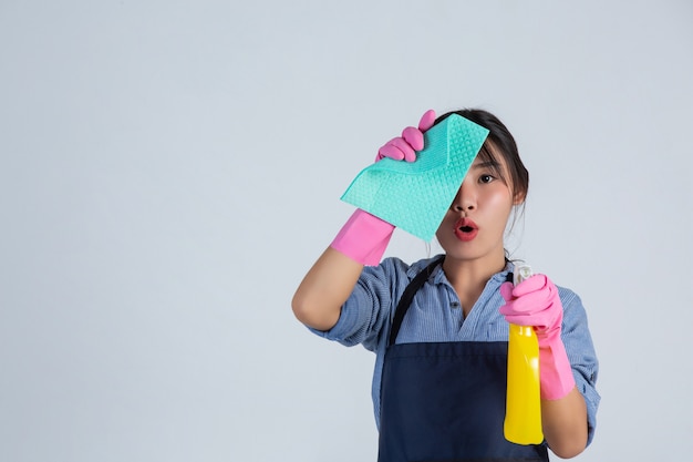 De jonge huisvrouw draagt gele handschoenen terwijl het schoonmaken met het product van schoon op witte muur.