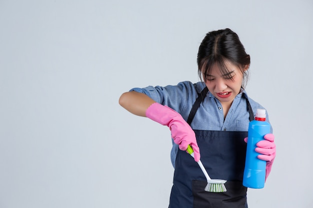 De jonge huisvrouw draagt gele handschoenen terwijl het schoonmaken met het product van schoon op witte muur.