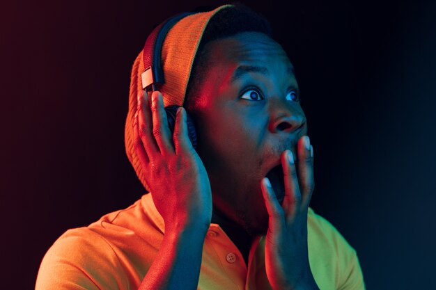De jonge knappe blij verrast hipster man luistert muziek met een koptelefoon op zwart met neonlichten