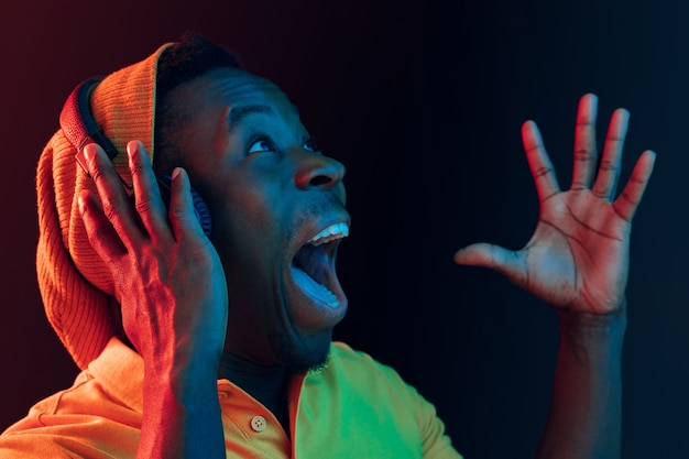 De jonge knappe blij verrast hipster man luistert muziek met een koptelefoon op zwart met neonlichten