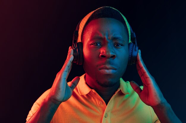 De jonge knappe ernstige trieste hipster man luisteren muziek met koptelefoon op zwart met neonlichten