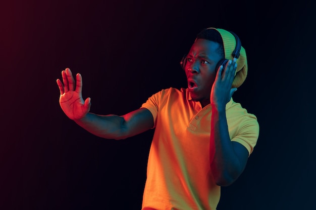 De jonge knappe gelukkig hipster man luisteren muziek met koptelefoon op zwart met neonlichten