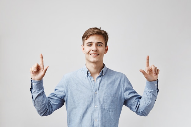 De jonge knappe mens kijkt omhoog, wijzend zijn vingers