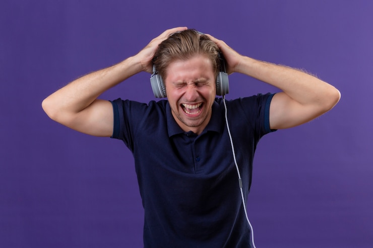 Gratis Foto de jonge knappe mens met hoofdtelefoons schreeuwt terwijl muziek met hoog volume luistert dat zich over purpere achtergrond bevindt
