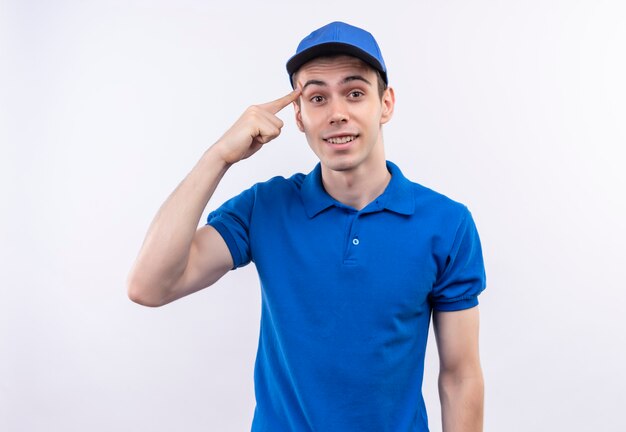 De jonge koerier die een blauw uniform en een blauwe pet draagt, denkt