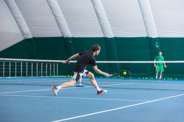 De jonge man in een gesloten tennisbaan met bal