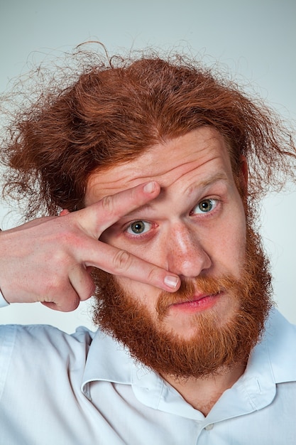 Gratis foto de jonge man met lang rood haar die camera bekijkt, zijn oog opent