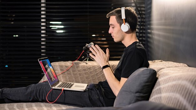 De jonge man van de maker van inhoud zit op zijn laptop op de bank tijdens de conferentie. Handen ineen. Werken vanuit huis