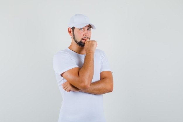 De jonge mens die terwijl hij kin op hand in t-shirt, GLB steunt en bezorgd kijkt. vooraanzicht.