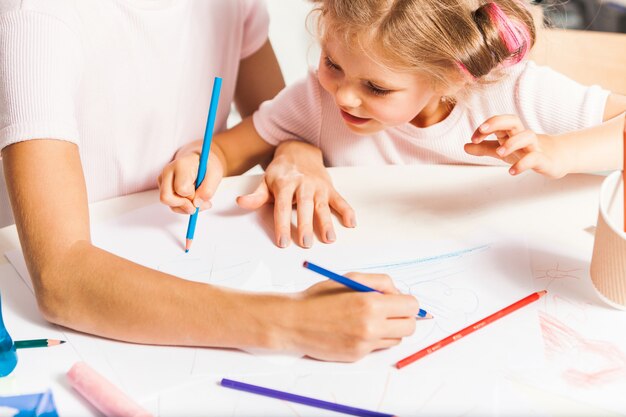 De jonge moeder en haar dochtertje tekenen met potloden thuis