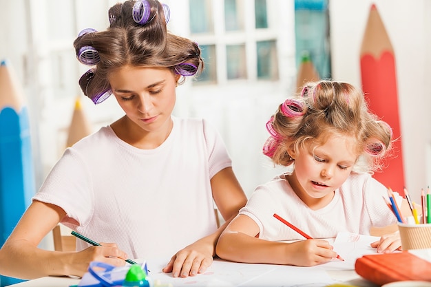 De jonge moeder en haar dochtertje tekenen thuis met potloden