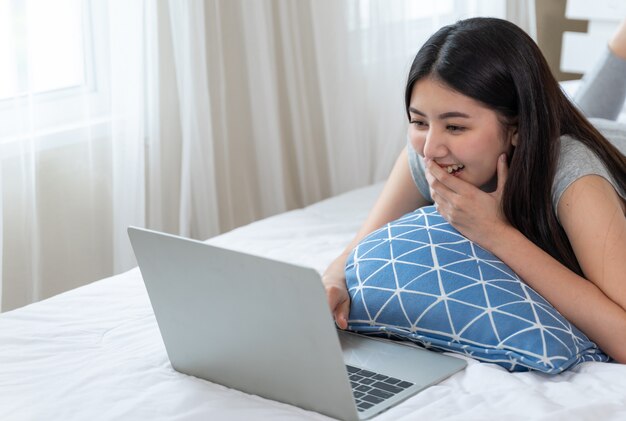 De jonge mooie vrouw vult gelukkige usiniglaptop computer op bed