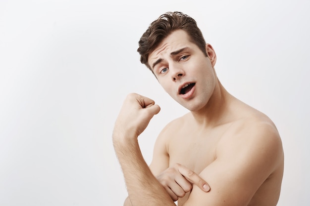 De jonge positieve spiermens met donker haar en blauwe ogen, toont bicepsen na geïsoleerde opleiding in gymnastiek ,. Knappe blanke man pronkt met kracht, toont sterke man de hand