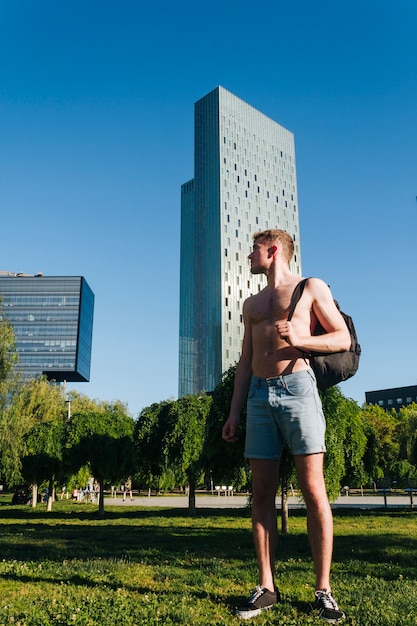 De jonge shirtless rugzak die van de mensenholding zich op gras in park bevinden