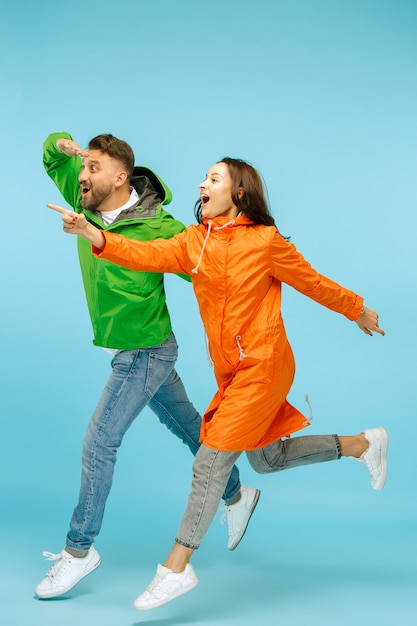 De jonge verrast paar in studio in herfst jassen geïsoleerd op blauw.