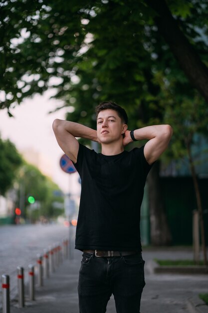 De jonge volwassen mens in een zwart t-shirt en jeans loopt op een stadsstraat op een zonnige dag