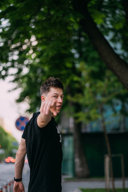 De jonge volwassen mens in een zwart t-shirt en jeans loopt op een stadsstraat