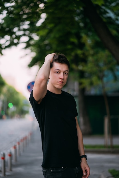 De jonge volwassen mens in een zwart t-shirt en jeans loopt op een stadsstraat