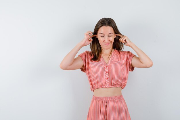 De jonge vrouw bedekt haar oren met wijsvingers op een witte achtergrond