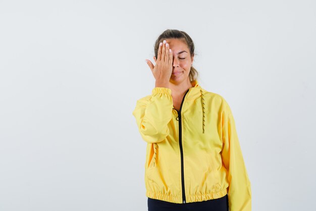 De jonge vrouw die haar één oog behandelt dient gele regenjas in