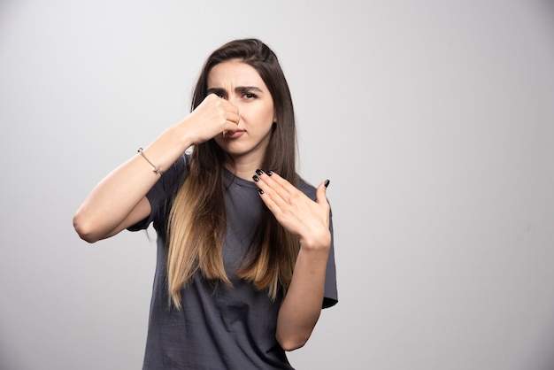 De jonge vrouw die haar neus behandelt met hand over een grijze achtergrond.