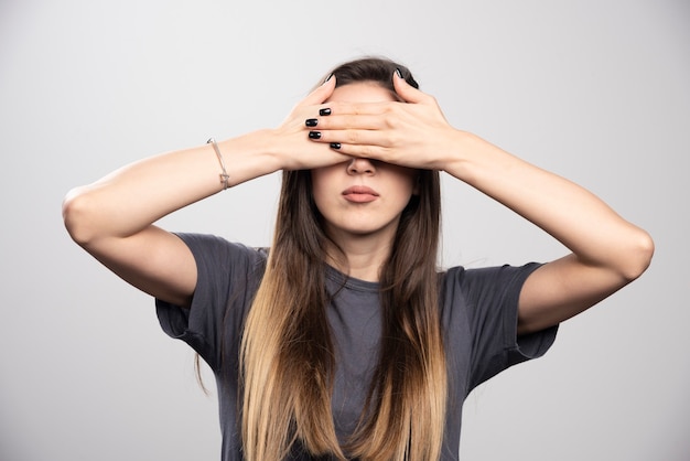 De jonge vrouw die haar ogen behandelt met handen over een grijze achtergrond.