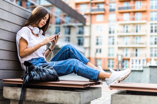 De jonge vrouw die mobiele telefoon met behulp van luistert muziek terwijl het zitten op bank in een park