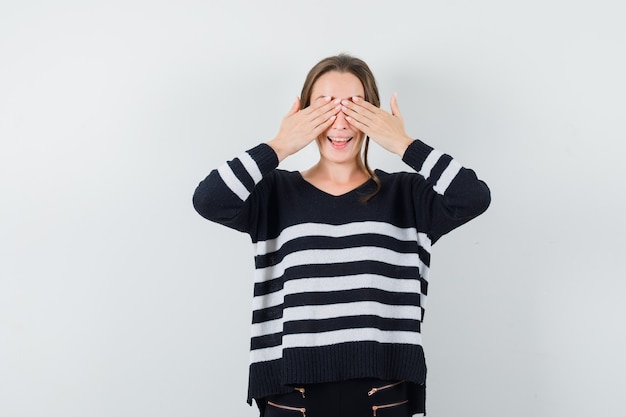 De jonge vrouw die ogen behandelt met beide dient gestreept breigoed en zwarte broek in en kijkt gelukkig