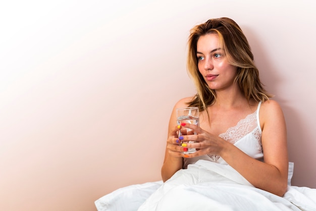 Gratis foto de jonge vrouw die van de close-up weg houdend een glas water in bed kijkt