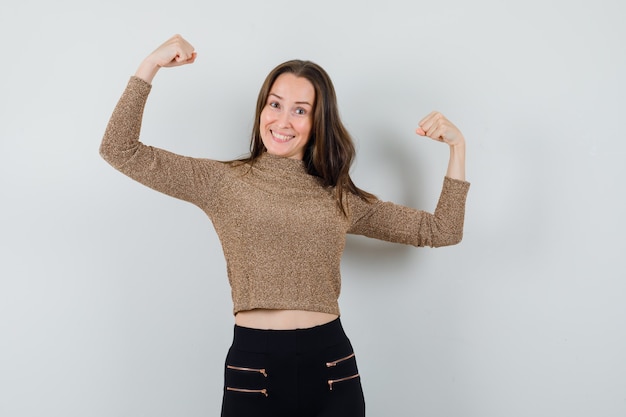 De jonge vrouw die winnaar toont stelt in goudvergulde sweater en zwarte broek en kijkt zelfverzekerd, vooraanzicht.