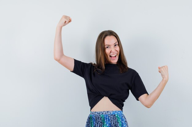 De jonge vrouw die winnaar toont stelt in zwart t-shirt en blauwe rok en ziet er aantrekkelijk uit